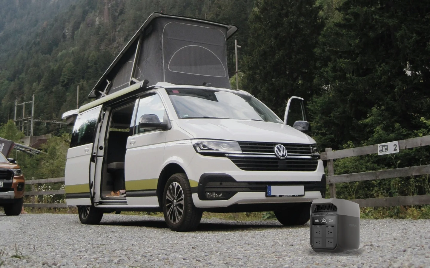 Illustrative scene: an EcoFlow DELTA 3 on level gravel beside a parked camper van in the mountains.